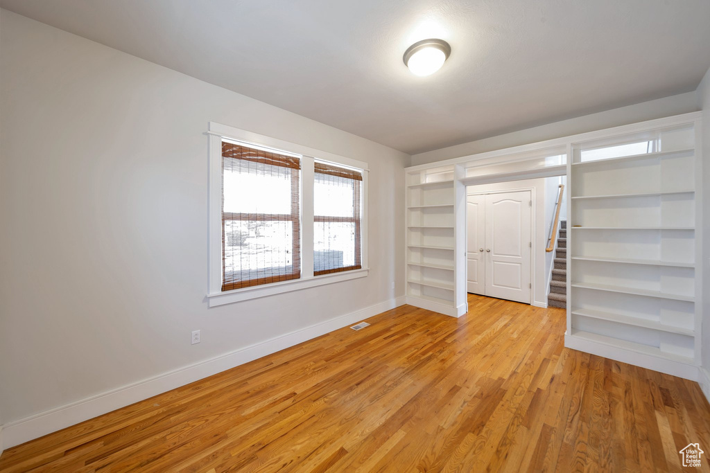 Empty room with light wood-type flooring, visible vents, built in features, and baseboards