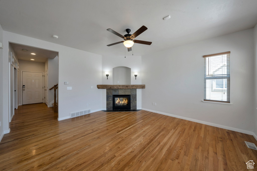 Unfurnished living room featuring baseboards, light wood-type flooring, visible vents, and a tiled fireplace