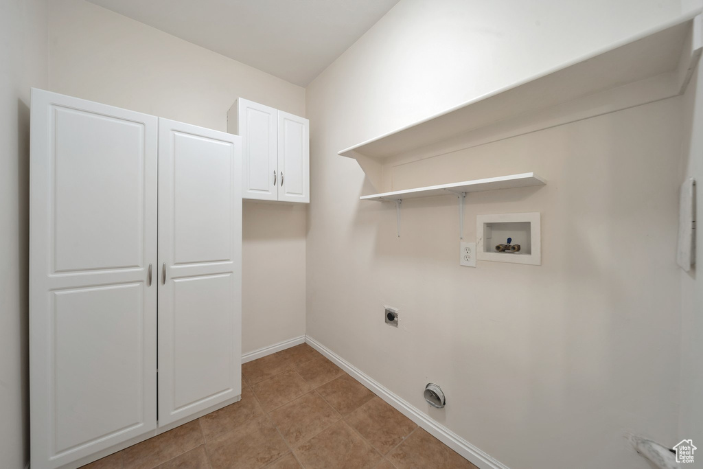 Laundry area featuring hookup for an electric dryer, light tile patterned flooring, baseboards, hookup for a washing machine, and cabinet space