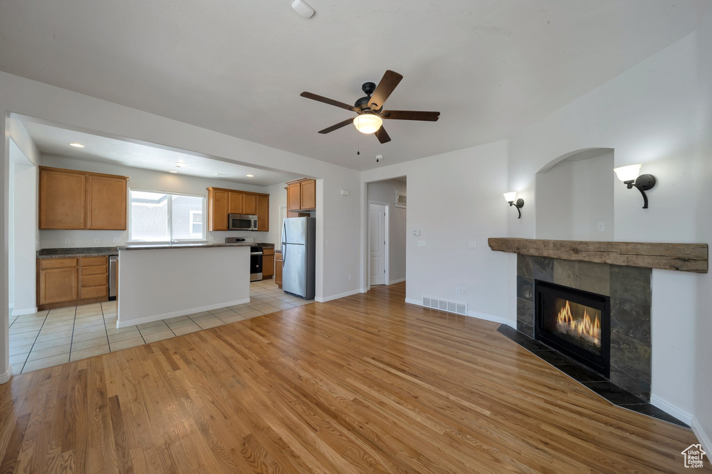 Unfurnished living room with ceiling fan, a tile fireplace, light wood-style flooring, baseboards, and visible vents