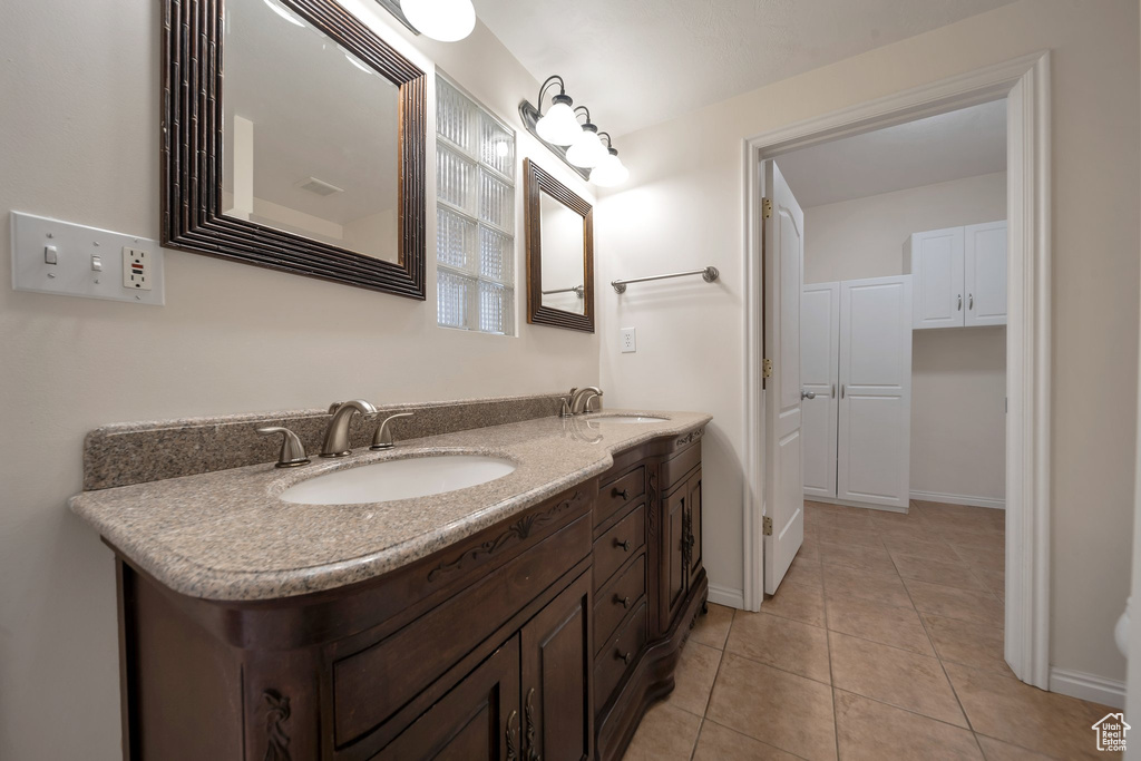 Bathroom with double vanity, tile patterned floors, baseboards, and a sink