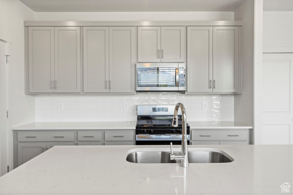 Kitchen with appliances with stainless steel finishes, gray cabinetry, light stone counters, and tasteful backsplash