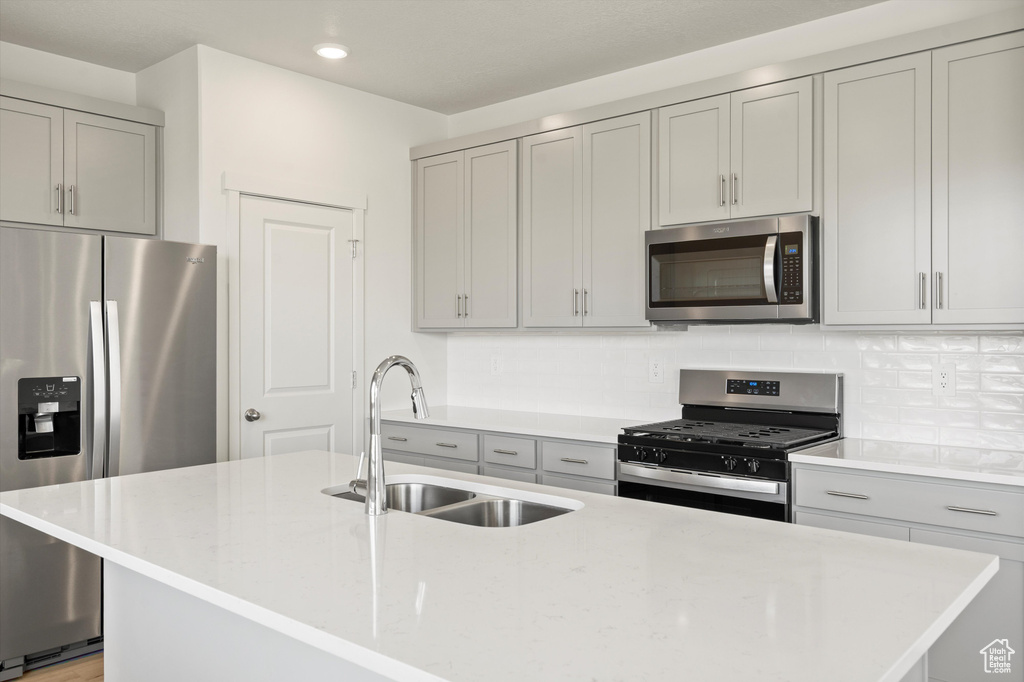 Kitchen with appliances with stainless steel finishes, gray cabinetry, tasteful backsplash, recessed lighting, and an island with sink