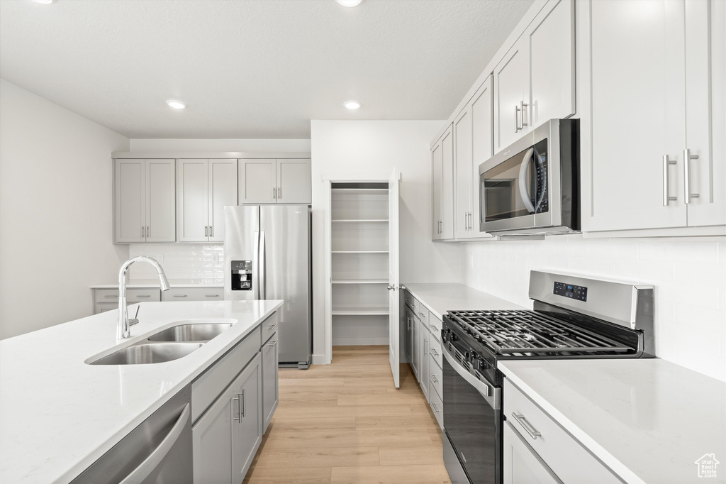 Kitchen with stainless steel appliances, light wood-style flooring, decorative backsplash, recessed lighting, and gray cabinetry