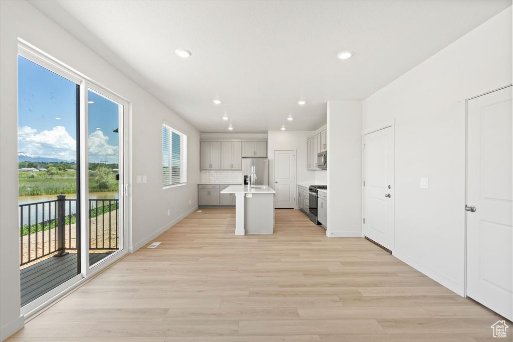 Kitchen with appliances with stainless steel finishes, light wood-style flooring, recessed lighting, a center island with sink, and light countertops