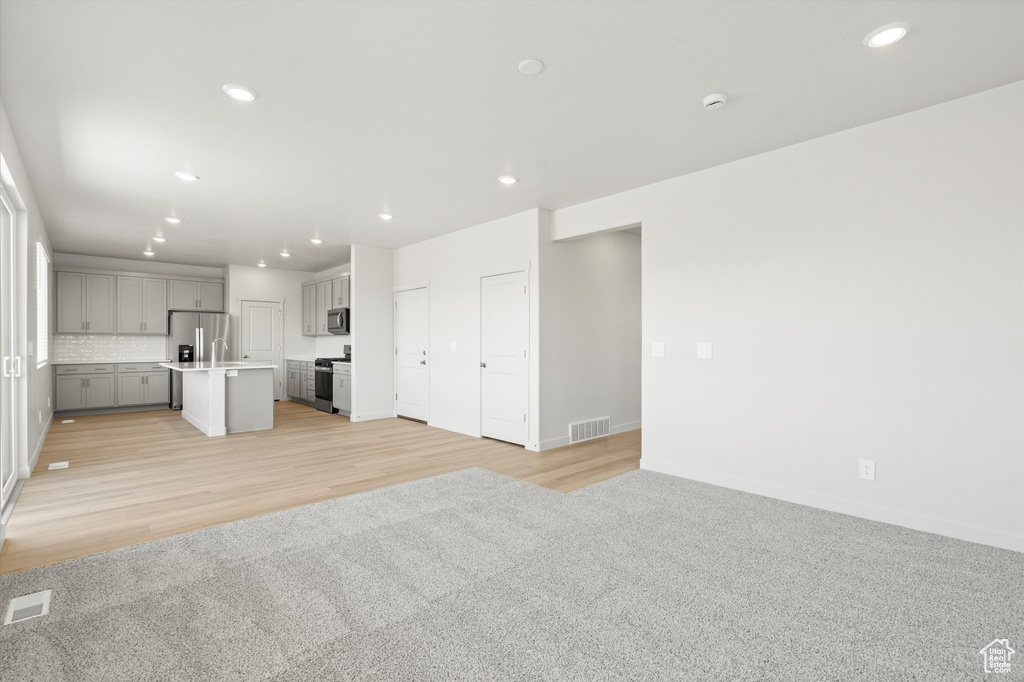 Unfurnished living room with recessed lighting, light wood finished floors, and light carpet