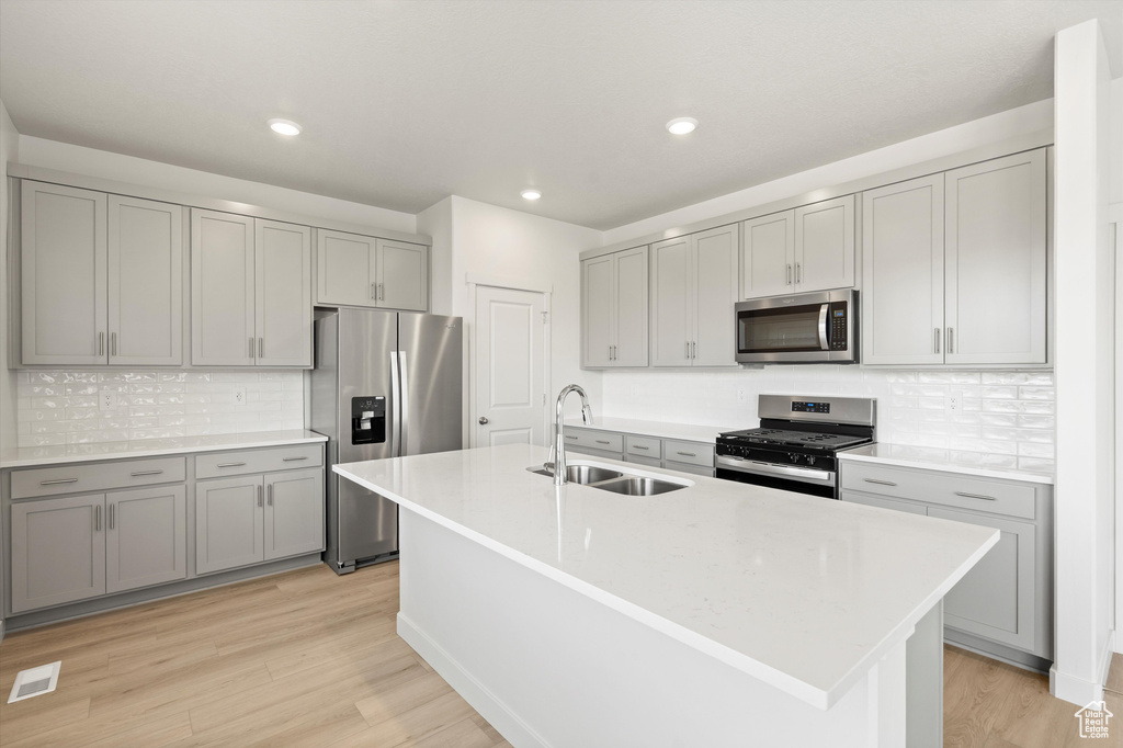 Kitchen featuring stainless steel appliances, gray cabinetry, tasteful backsplash, light wood-style flooring, and light countertops