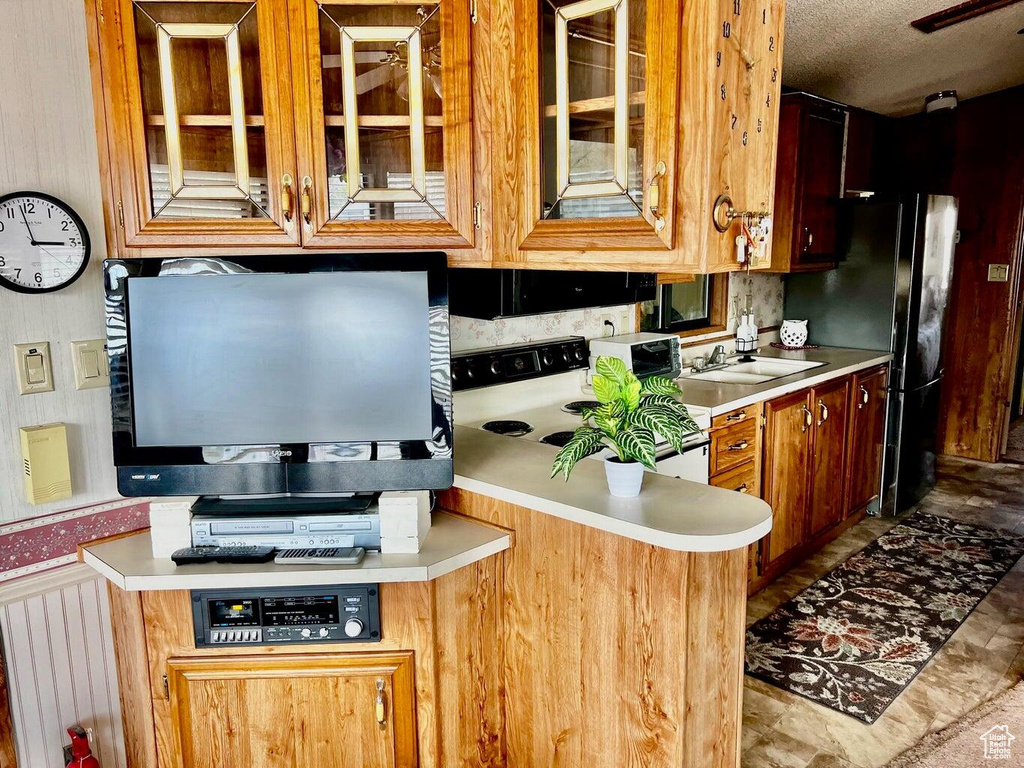 Kitchen featuring light countertops, electric range oven, glass insert cabinets, and freestanding refrigerator