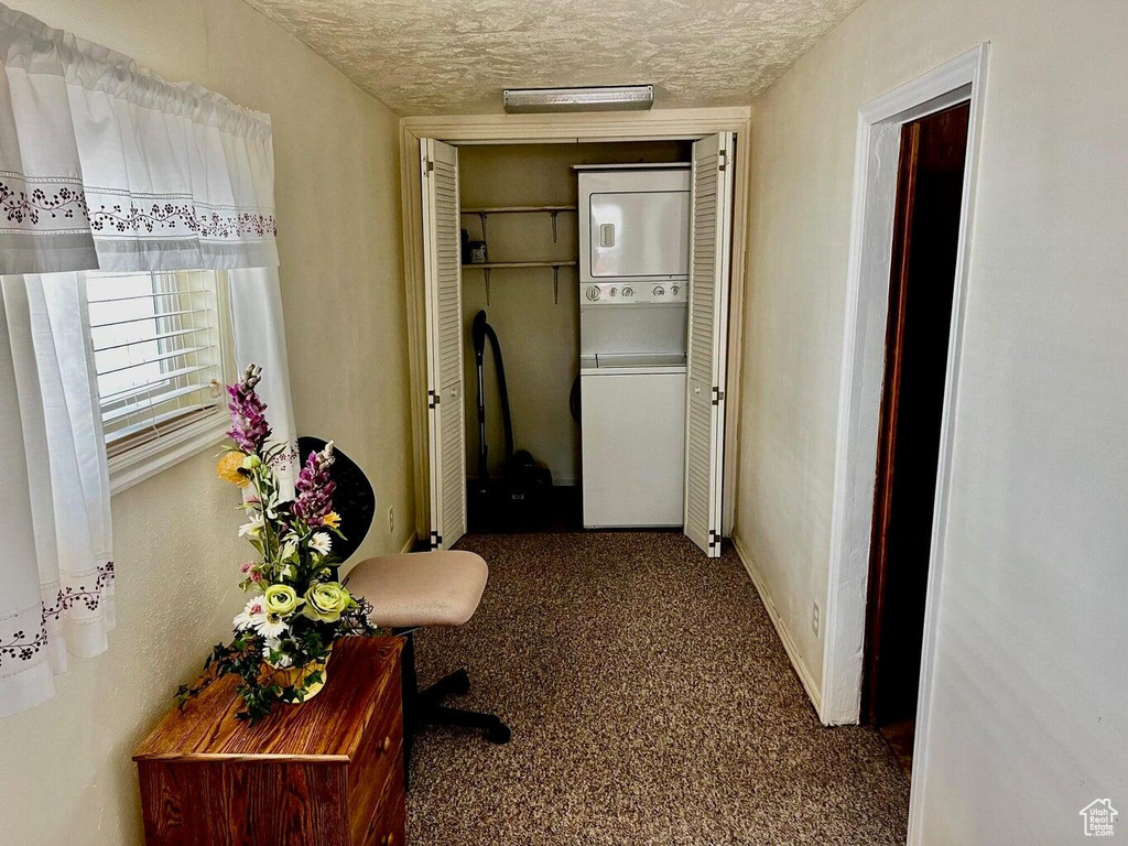 Corridor with baseboards, carpet floors, stacked washer and clothes dryer, and a textured ceiling