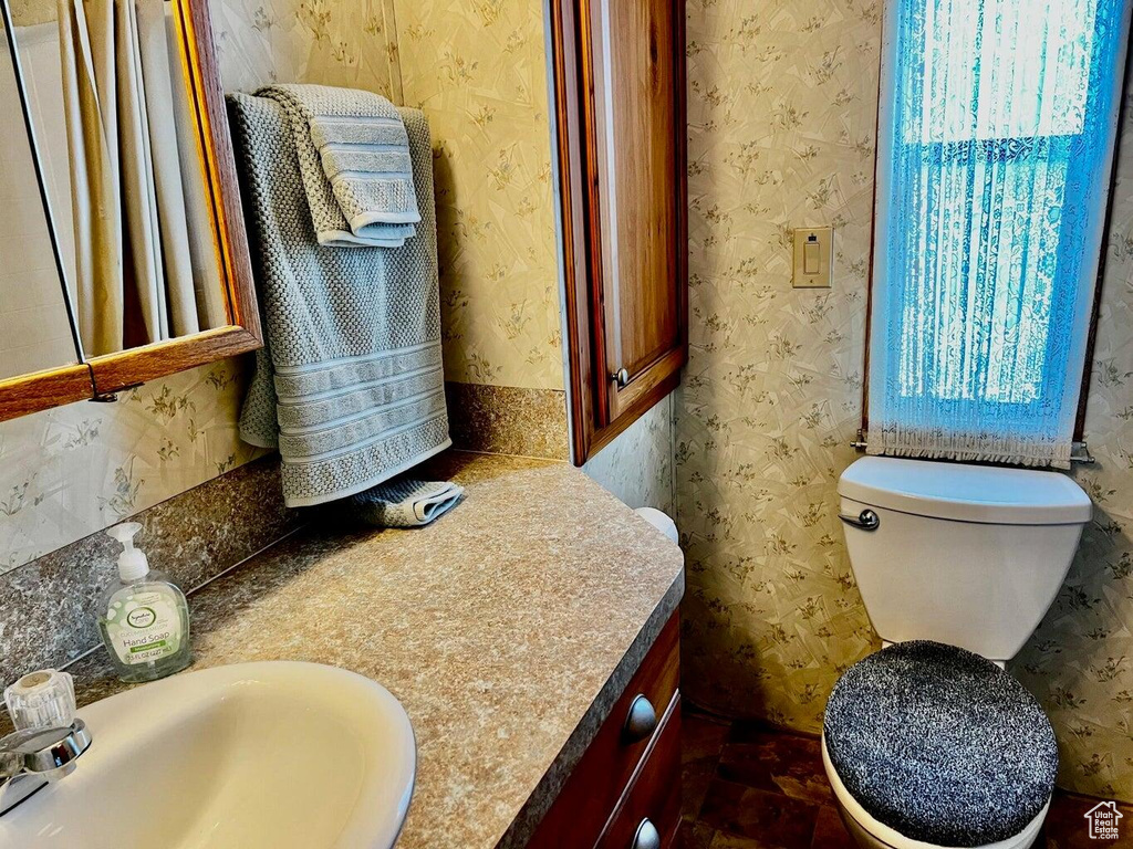 Bathroom featuring toilet, vanity, and wallpapered walls