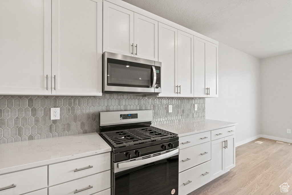 Kitchen featuring appliances with stainless steel finishes, light wood-type flooring, white cabinetry, decorative backsplash, and light stone countertops