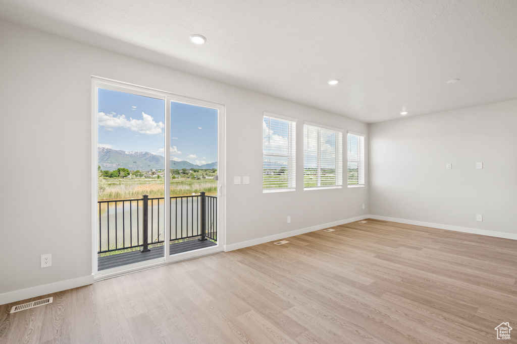 Unfurnished room with light wood-type flooring, baseboards, a water and mountain view, and recessed lighting