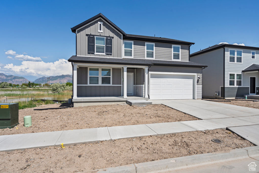 View of front of house featuring a porch, board and batten siding, driveway, a garage, and a water and mountain view