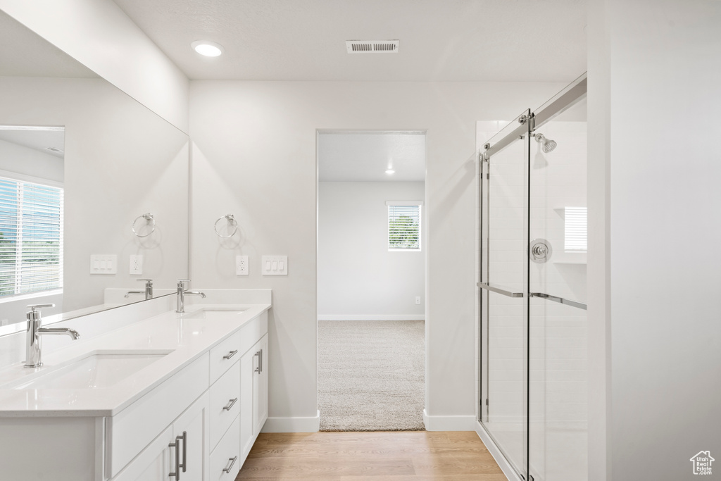 Bathroom featuring double vanity, a tile shower, wood finished floors, baseboards, and recessed lighting