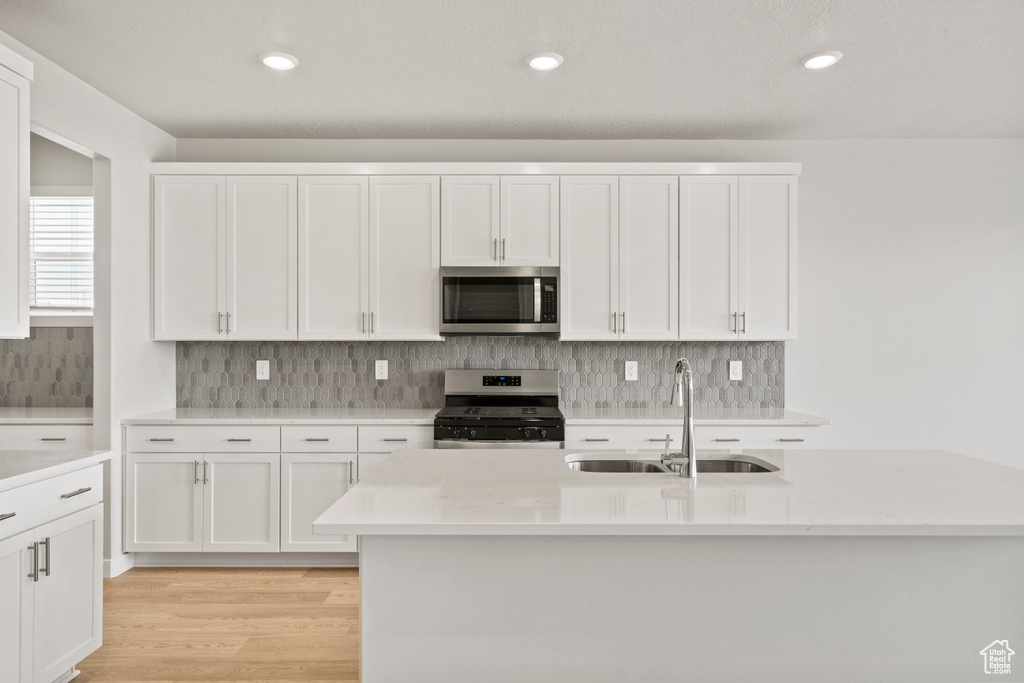 Kitchen with stainless steel appliances, a sink, light wood finished floors, white cabinets, and recessed lighting