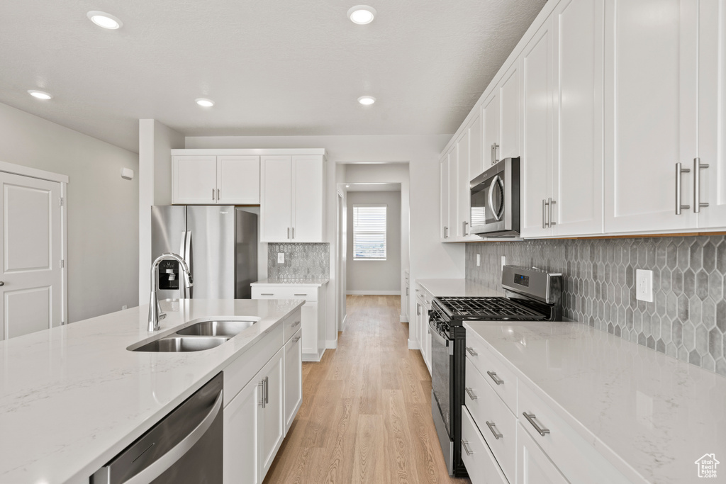 Kitchen with stainless steel appliances, a sink, light wood-style flooring, white cabinets, and recessed lighting