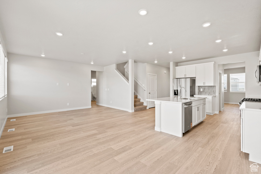 Kitchen featuring stainless steel appliances, light wood-style floors, white cabinets, an island with sink, and light countertops