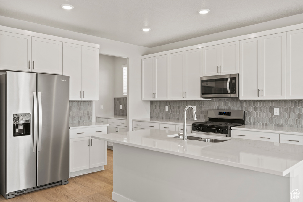 Kitchen featuring appliances with stainless steel finishes, a sink, light wood finished floors, an island with sink, and white cabinetry