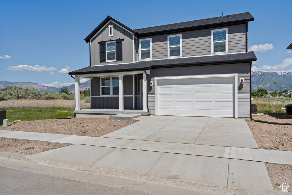 View of front of property with a mountain view, concrete driveway, a garage, a porch, and central AC