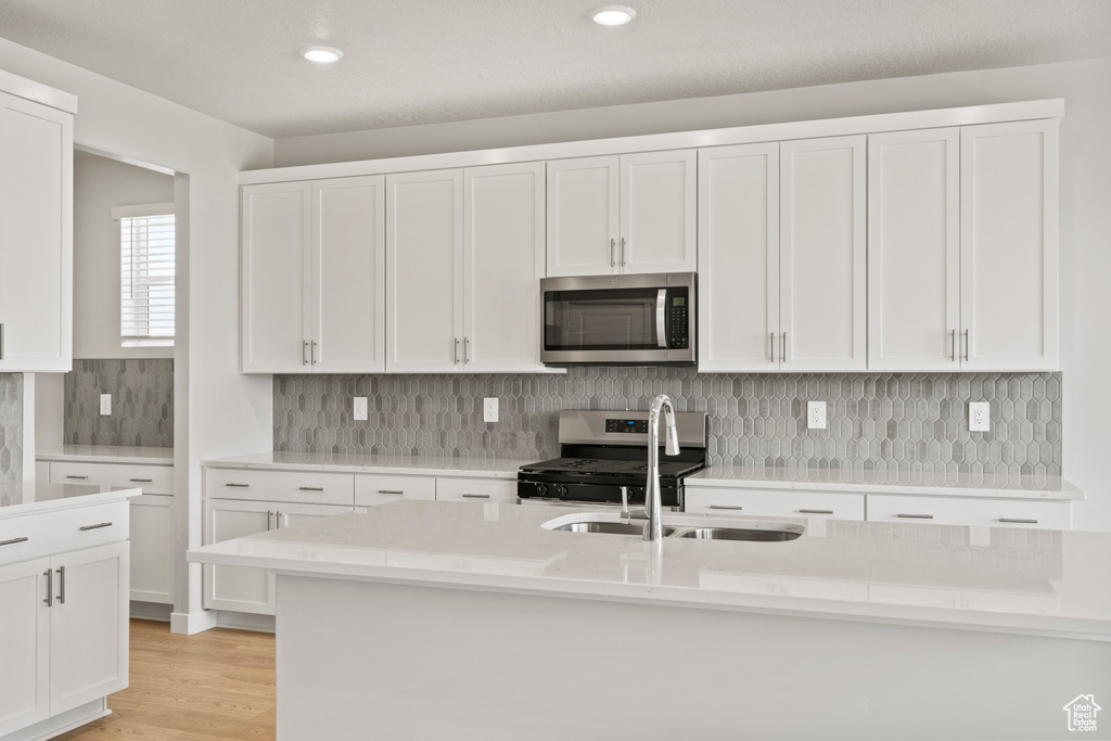 Kitchen with appliances with stainless steel finishes, a sink, light countertops, white cabinetry, and tasteful backsplash