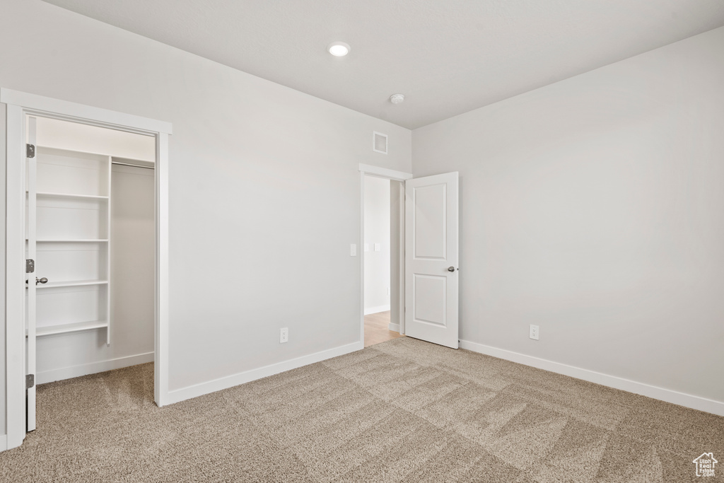 Unfurnished bedroom featuring carpet flooring, a walk in closet, and baseboards