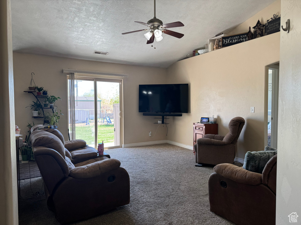 Carpeted living area with a textured ceiling, vaulted ceiling, baseboards, visible vents, and a ceiling fan