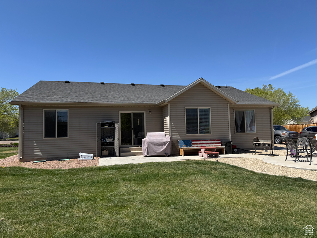 Rear view of property featuring a lawn, a shingled roof, and a patio