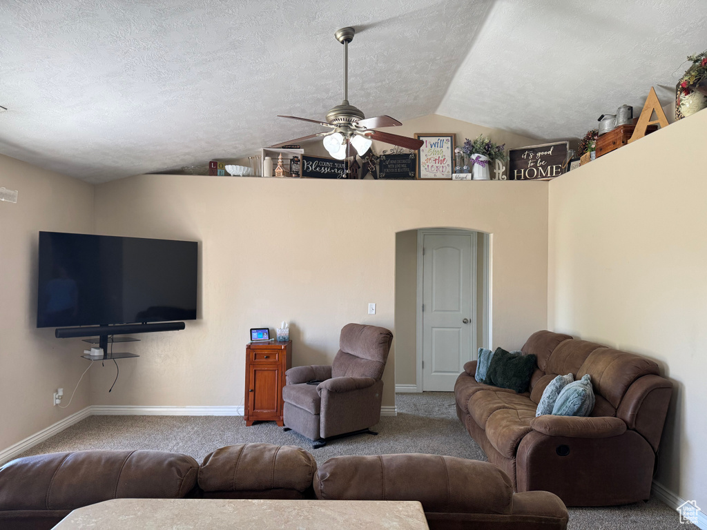 Living room with vaulted ceiling, a ceiling fan, a textured ceiling, carpet floors, and baseboards