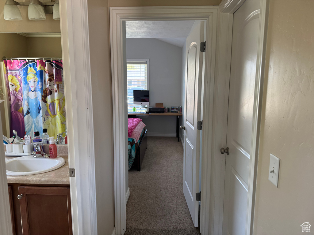 Hallway featuring carpet, vaulted ceiling, baseboards, and a sink