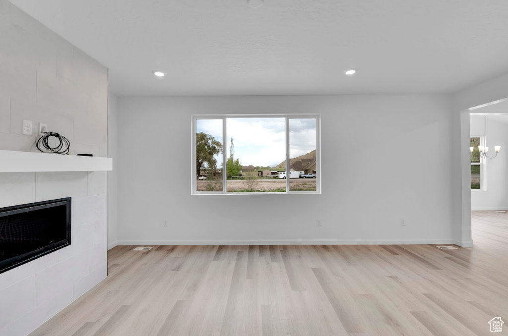 Unfurnished living room with wood finished floors, a tiled fireplace, a chandelier, recessed lighting, and baseboards