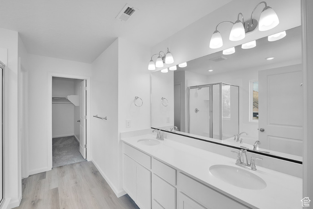 Bathroom featuring a shower stall, wood finished floors, a walk in closet, double vanity, and baseboards