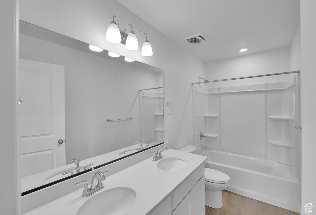 Full bathroom with toilet, wood finished floors, shower / bathtub combination, and double vanity