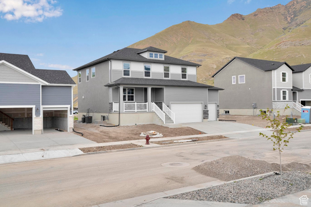 View of front of home featuring concrete driveway, a garage, a porch, central AC unit, and a mountain view