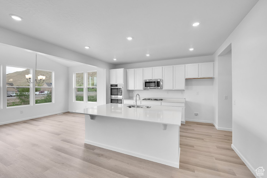 Kitchen with stainless steel microwave, a sink, white cabinetry, light wood finished floors, and baseboards
