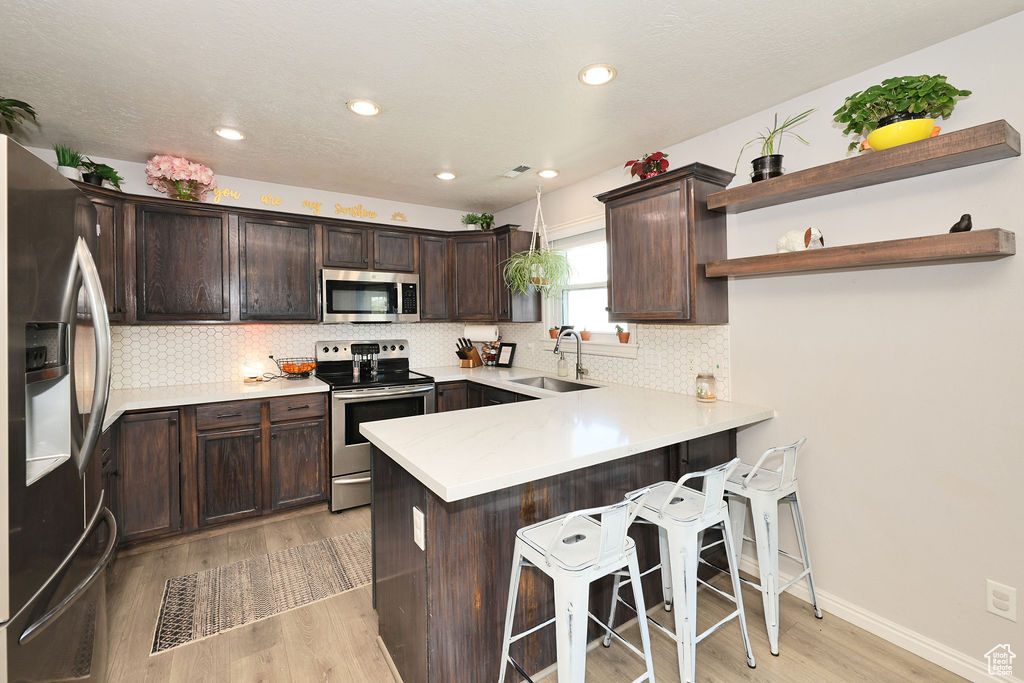 Kitchen with a sink, light wood-style floors, dark brown cabinetry, a peninsula, and appliances with stainless steel finishes