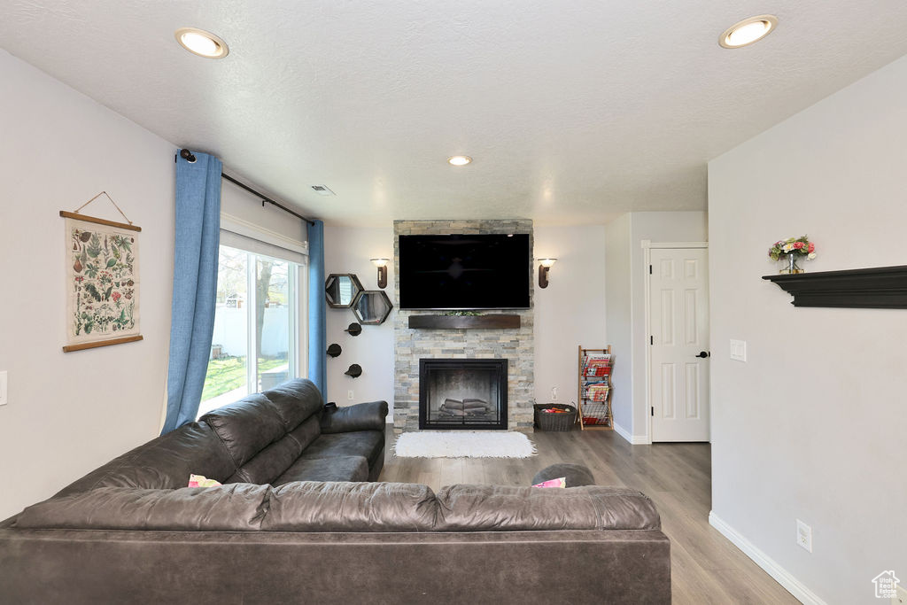 Living area with visible vents, baseboards, recessed lighting, wood finished floors, and a stone fireplace