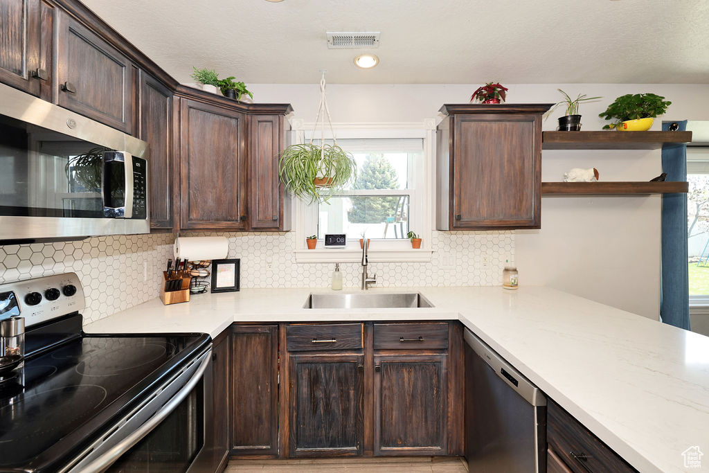 Kitchen featuring stainless steel appliances, a sink, tasteful backsplash, dark brown cabinets, and open shelves