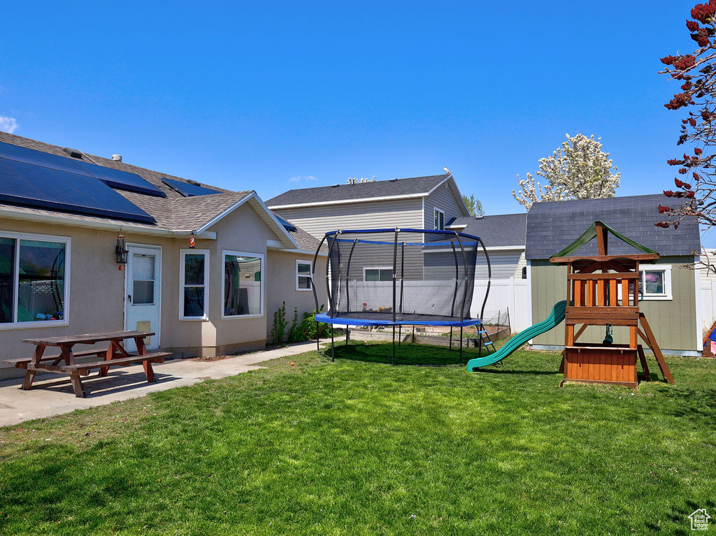 View of yard with a trampoline, a patio area, a playground, and fence