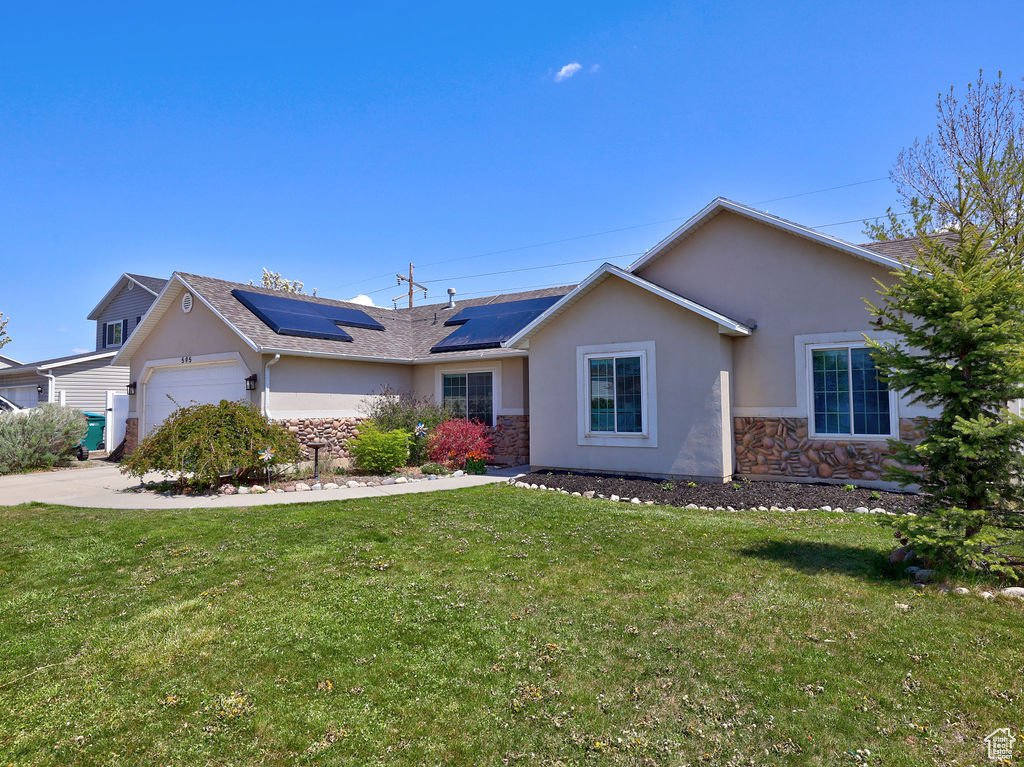 Ranch-style home with stucco siding, roof mounted solar panels, a front yard, and a garage