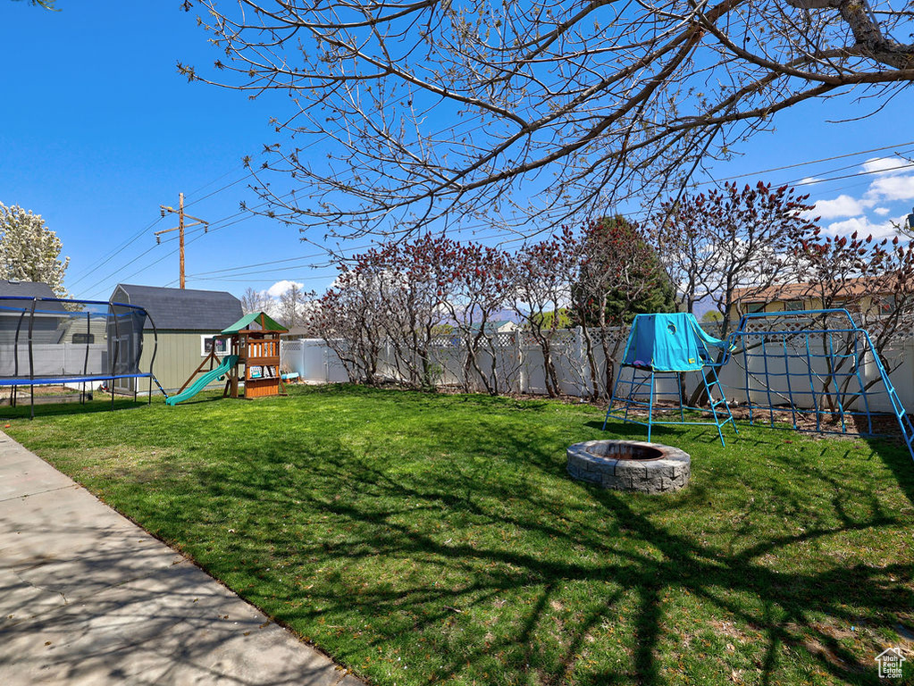 View of yard with a fenced backyard, a fire pit, a playground, and a trampoline