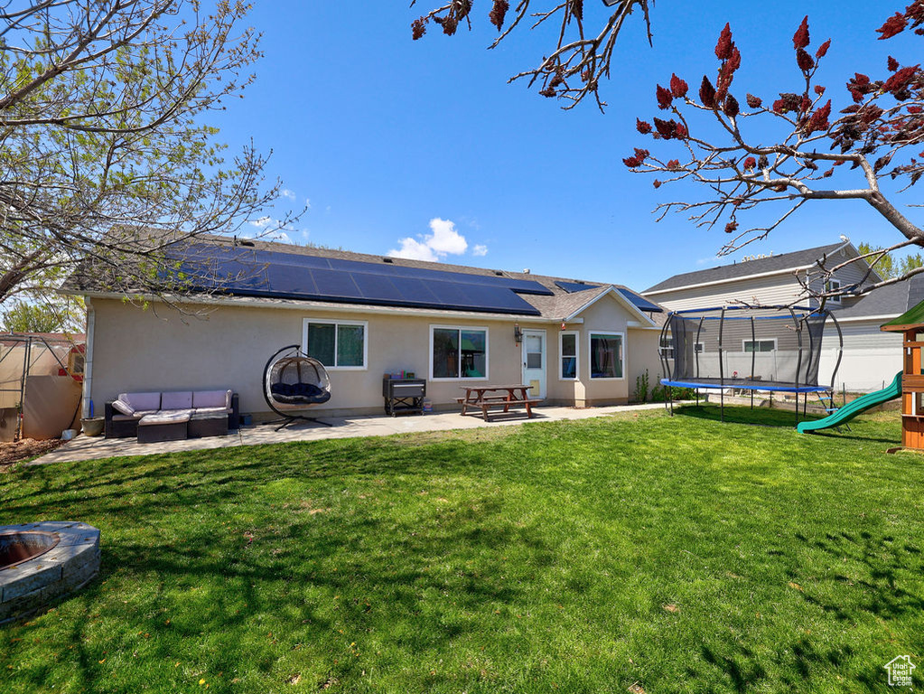 Rear view of property with a playground, a trampoline, roof mounted solar panels, a patio, and stucco siding