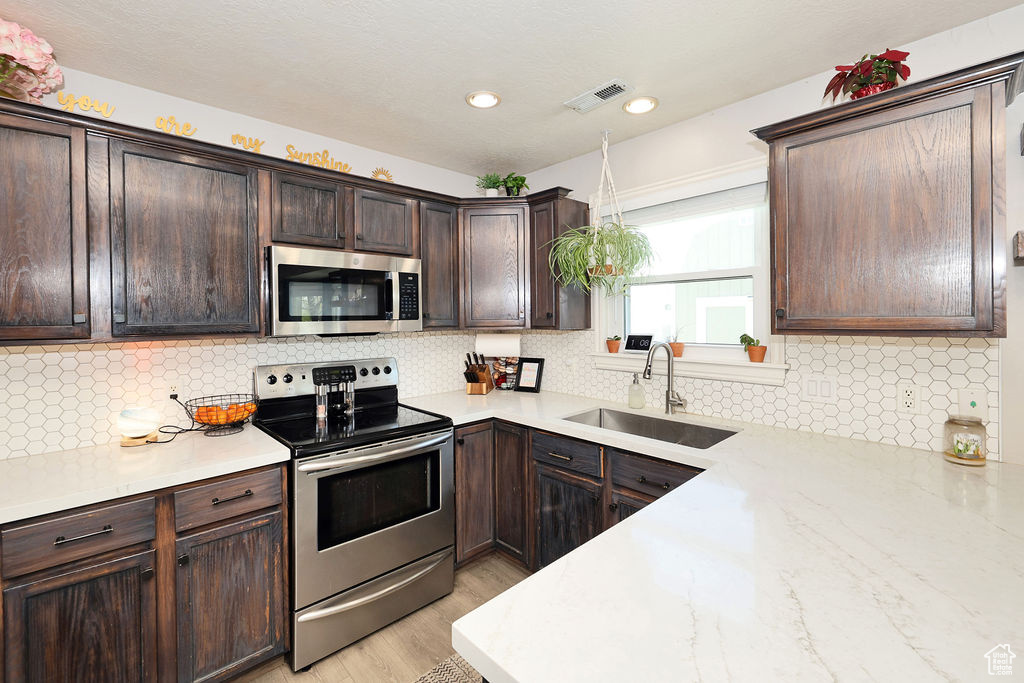 Kitchen with dark brown cabinets, stainless steel appliances, visible vents, and a sink