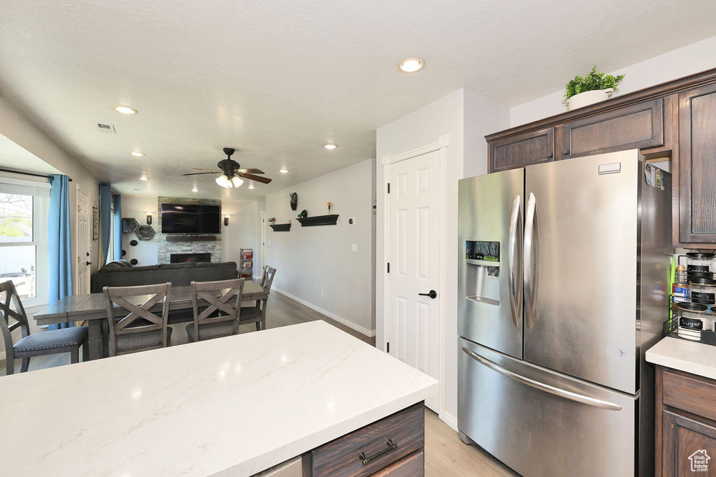 Kitchen featuring dark brown cabinets, light wood-style floors, a ceiling fan, stainless steel refrigerator with ice dispenser, and a fireplace