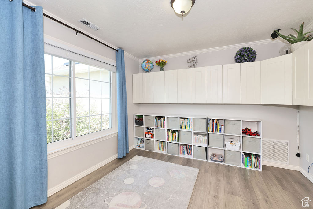 Rec room featuring baseboards, crown molding, wood finished floors, and visible vents
