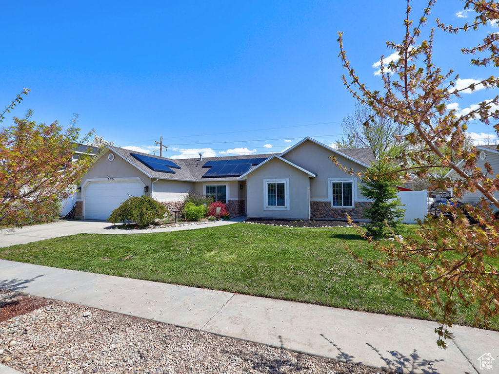 Ranch-style house with solar panels, stone siding, a garage, a front yard, and stucco siding