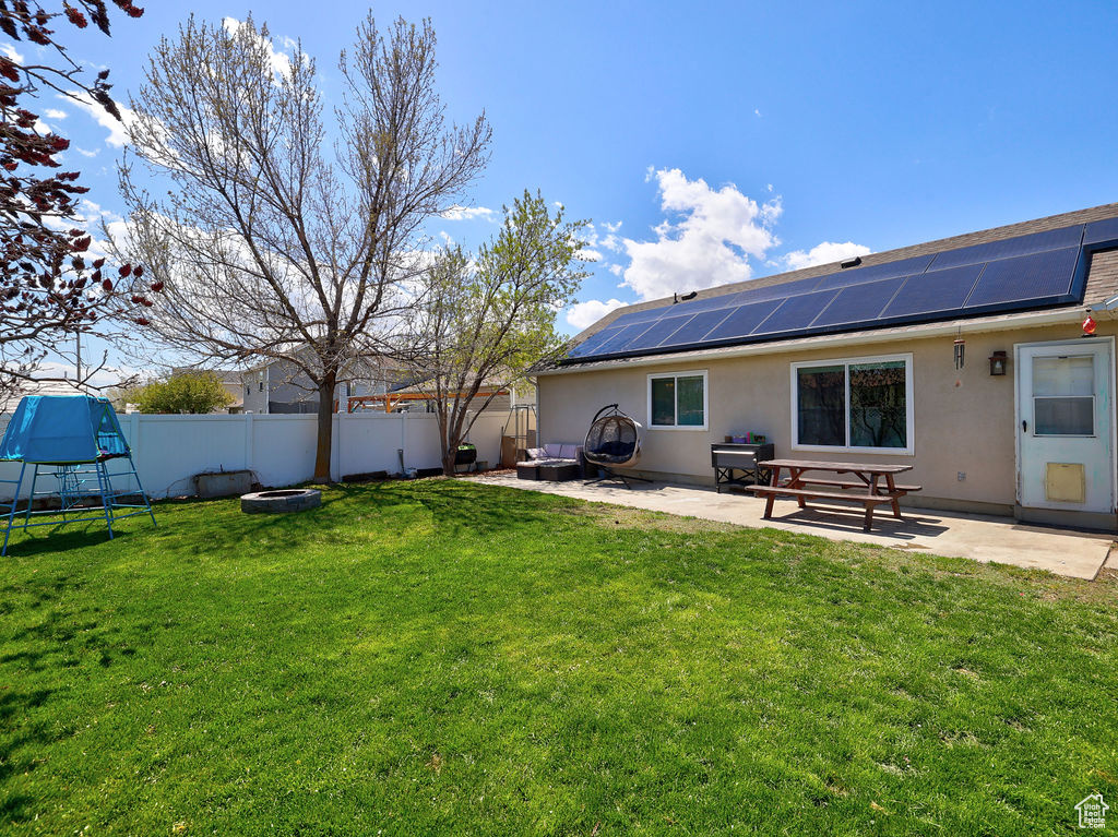 Back of property featuring a fire pit, solar panels, a patio area, and a fenced backyard