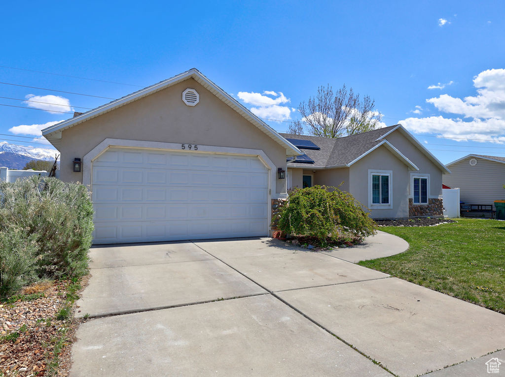 Ranch-style house with concrete driveway, an attached garage, roof mounted solar panels, a front yard, and stucco siding