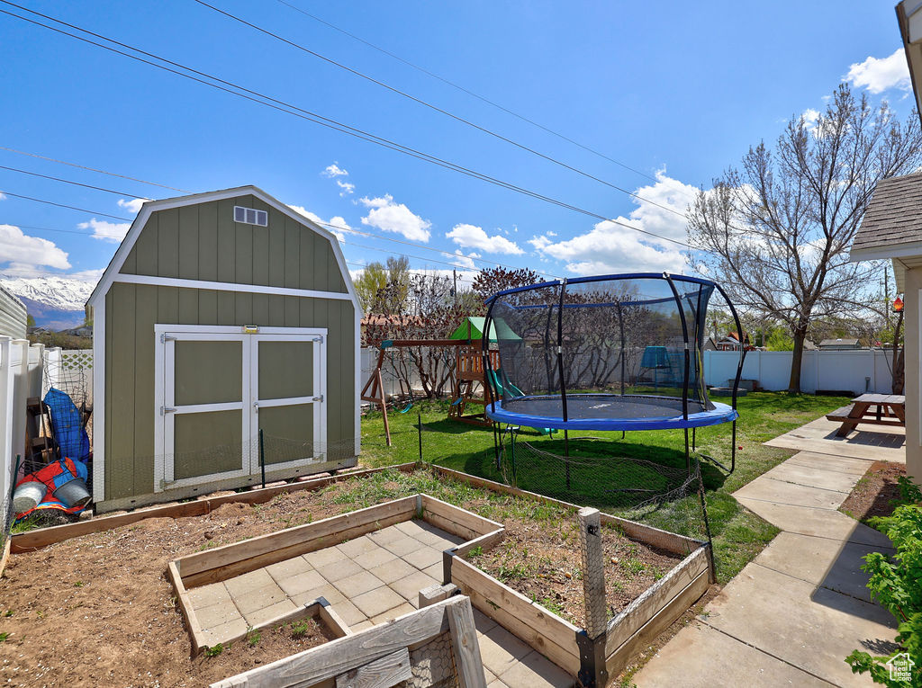 View of yard with a storage unit, a garden, an outbuilding, a fenced backyard, and a trampoline