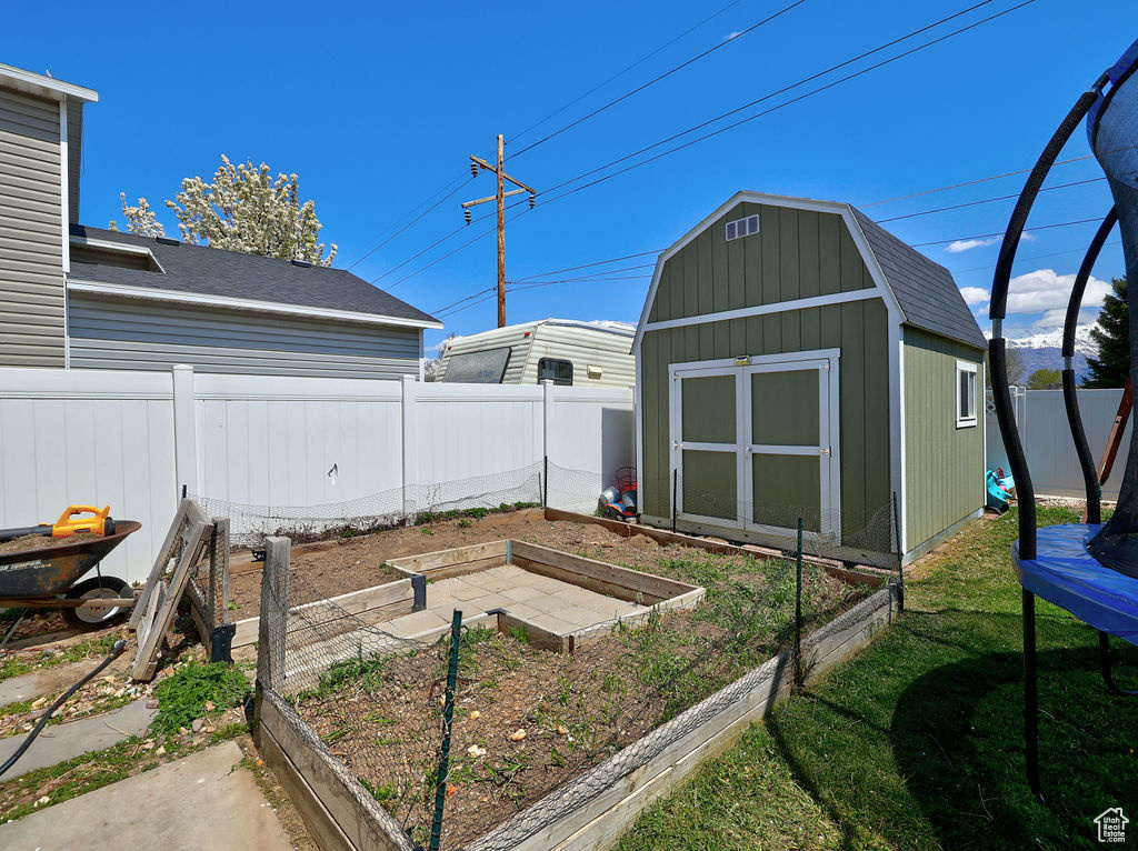 View of yard with a fenced backyard, a garden, a storage shed, an outdoor structure, and a trampoline