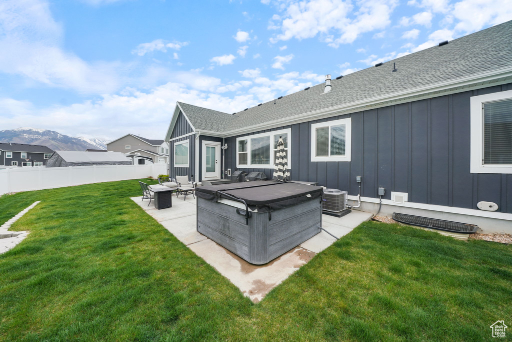 Rear view of property featuring a patio, a hot tub, board and batten siding, and roof with shingles